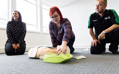 Woman practices using a defibrillator on a training manikin during a first aid training course.
