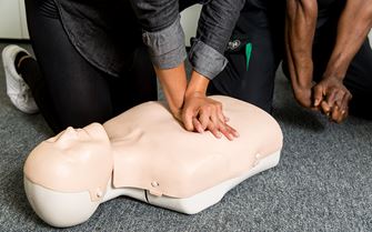 Woman practices CPR using a training manikin during a first aid course.
