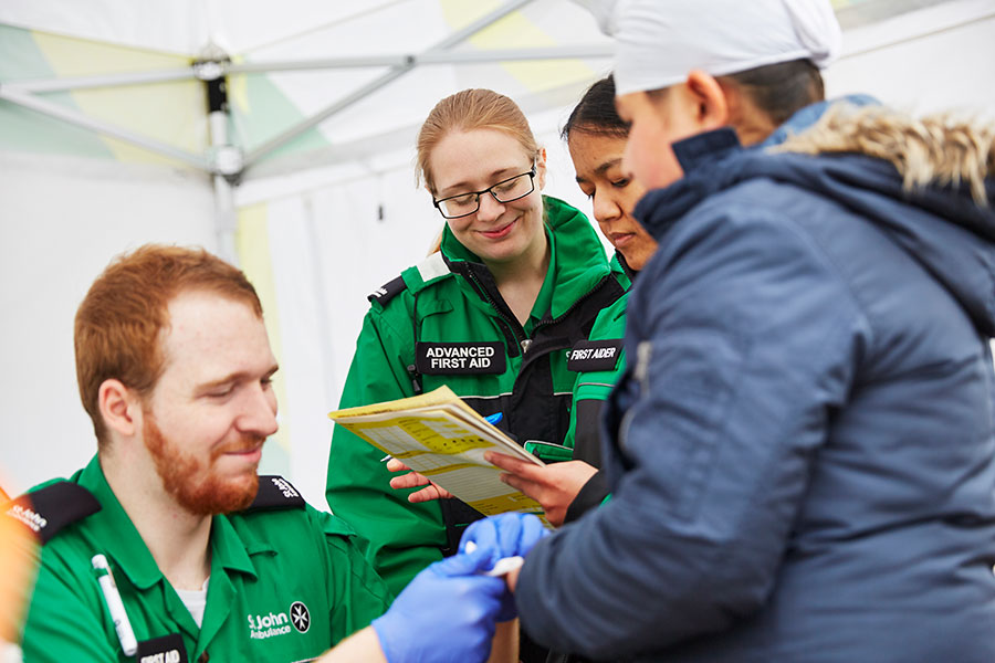 Volunteers treating patient's finger and completing paperwork in a mobile treatment centre at an event. 