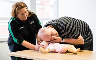 First aid course participant practices CPR using a baby mannequin